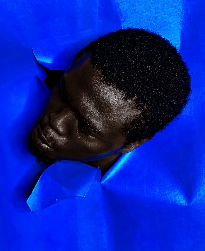 Surreal art portrait of a man's head emerging from vibrant blue paper.