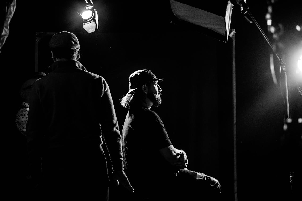 A black and white portrait of individuals in a dramatic studio setting with focused lighting.