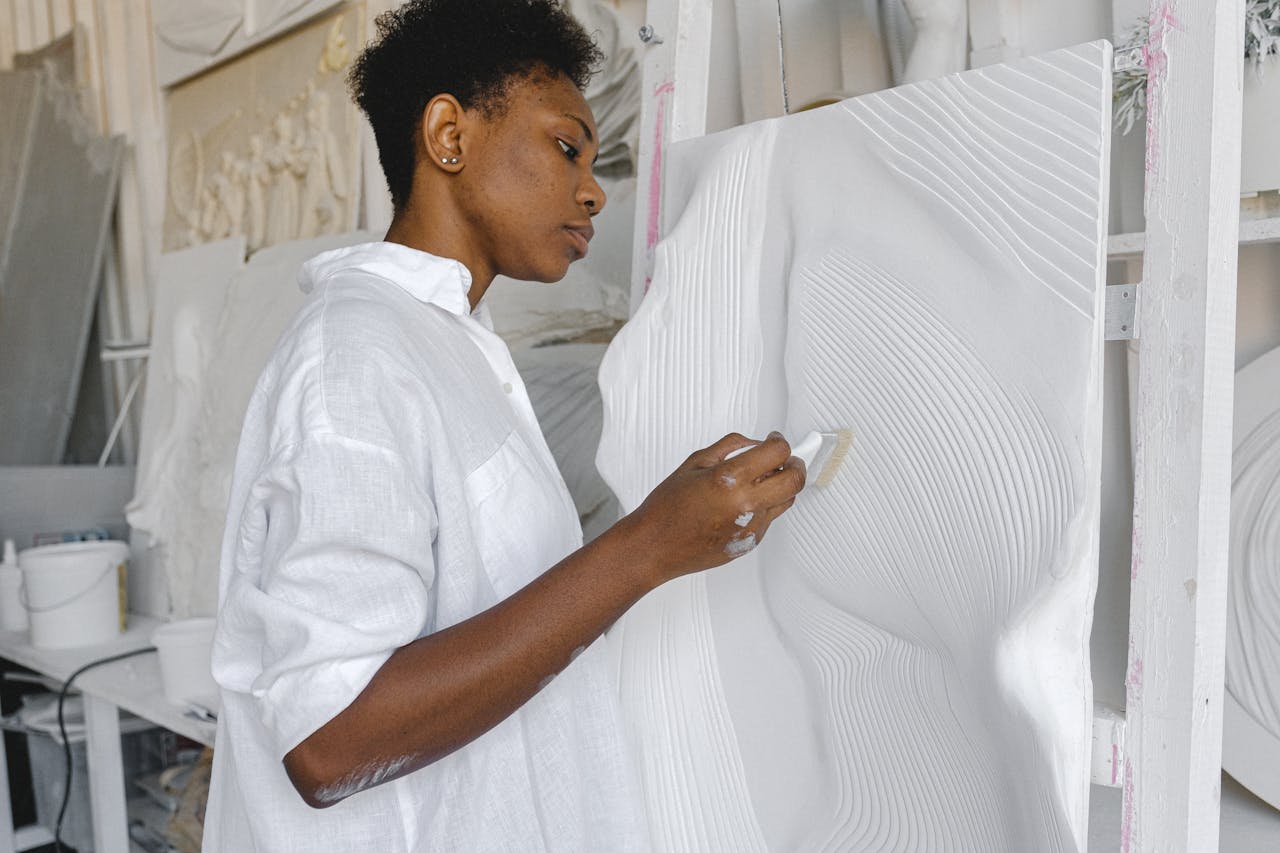 A focused artist in a studio works on a textured white artwork with precision.